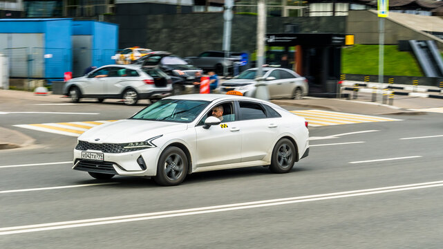 White car Kia K5 Fifth generation DL3 speed driving on asphalt city road at daytime. City taxi car with checkers on roof