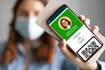 Young girl wearing a face mask holding a passport, ticket pass and smartphone with digital health passport app for travel during covid-19 pandemic.