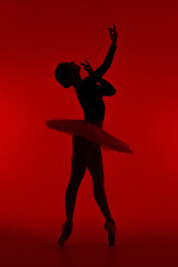 Fototapeta na wymiar Beautiful silhouette of ballerina on red background dancing ballet. Woman performs smooth movements with hands. Sensual dancer in tutu dress on scene under infrared light.. 