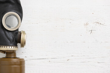 Closeup of a vintage black rubber gas mask on a white wooden background. Side view of a gas mask...