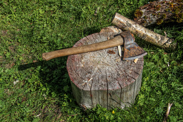 The axe is lying on a wooden, round stump. Rusty axe and firewood top view.An axe with firewood is...