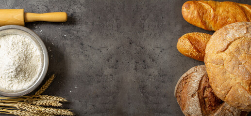 flour in an iron bowl and a rolling pin on a dark table top, freshly baked bread, baking ingredient, background with place for text