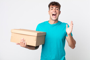 young handsome man feeling happy and astonished at something unbelievable and holding a cardboard...