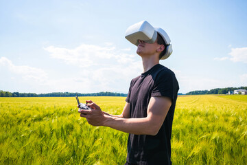 Man flying a drone with virtual reality glasses outside in nature on a wheat farming field.