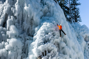 Male athlete climb cliff covered with ice, swinging the ice axe and using crampons to get a foothold