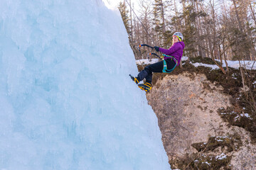 Female ice climber descending down an ice waterfall, stepping backward by kicking crampons right...
