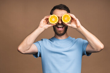 Healthy food and diet concept. Portrait of young bearded smiling man holding an orange fruit isolated on beige background.