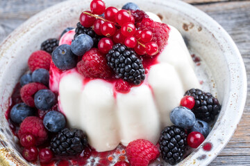 Modern style traditional blancmange almond pudding with wild berry coulis served as close-up in a Nordic design plate on a wooden board