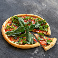 Sliced vegetarian pizza with spinach, tomatoes and olives. Vitamin Italian pizza with herbs and vegetables on gray background. Copy space.