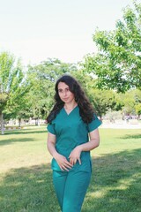 Portrait of healthcare worker / intern doctor / medical student woman of Turkish ethnicity confident in nature background, courtyard of hospital with green scrubs *3