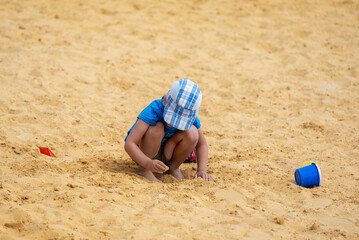 Fototapeta na wymiar Little boy plays in the yellow sand on the beach.