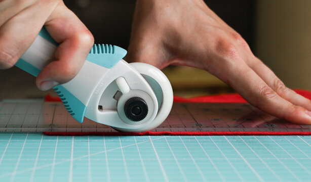 Closeup of a tailor cutting red fabrics using roller knife. Tools for sewing concept.