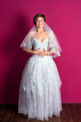 Fototapeta premium Bride on pink background. Woman dressed in wedding dress with lace, copyspace for text