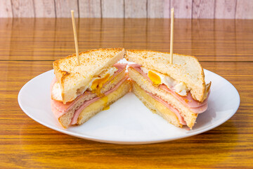 Double-decker sandwich for breakfast or a snack with a fried egg, several slices of ham and melted cheese and the sliced bread passed through the grill