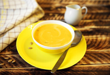 Pumpkin soup in a yellow plate on a wooden background.