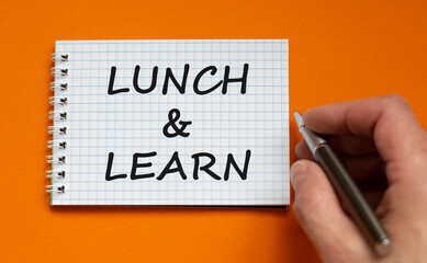 Lunch and learn symbol. Businessman writing words 'Lunch and learn' on white note. Beautiful orange background. Business, educational and lunch and learn concept. Copy space.