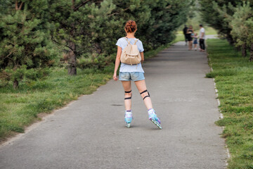 A young woman roller skating in a park on summer day.