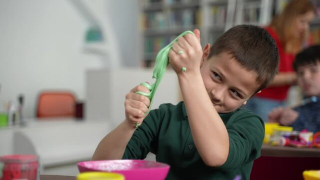 Elementary age autistic boy stretching hand-made slime during inclusive master class for children with different disabilities. Kids with special needs spending time making slimes on their own