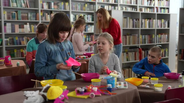 Two preteen autistic girls playing hand-made slimes sitting next to disabled boy wth cerebral palsy. Kids with different disabilities enjoying gaming activity at inclusive masterclass