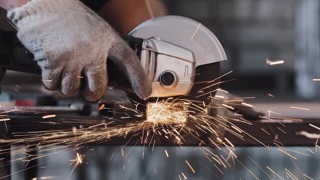 Manufacturing plant - man worker cuts off the part of metal detail with angle saw