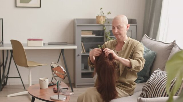 Medium shot of hairless mature woman suffering oncology putting on wig at home, smiling to her reflection in mirror