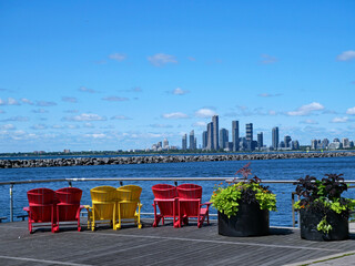 Colorful chairs on Toronto's waterfront boardwalk, with a view  of modern condominium apartment buildings in the west - obrazy, fototapety, plakaty