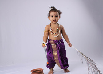 adorable Indian baby in krishna kanha or kanhaiya dress posing with his flute and peacock feather...