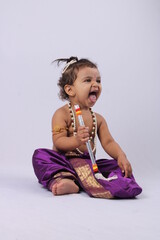 adorable Indian baby in krishna kanha or kanhaiya dress posing with his flute and peacock feather on white background. standing pose