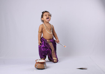 Janmashtami concept- adorable Indian baby in krishna kanha or kanhaiya dress posing with his flute and dahi handi (pot with curd) on white background. standing pose - obrazy, fototapety, plakaty
