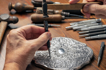 CRAFTSMAN'S HAND EMBOSSING METAL WITH PUNCH AND HAMMER IN THE WORKSHOP. SILVERSMITH, JEWELLERY AND HANDICRAFTS CONCEPT.