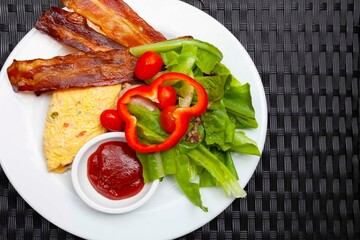 Western breakfast, scrambled eggs, bacon and fresh vegetables with tomato sauce