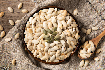 Dry pumpkin seeds in bowl on wooden table.