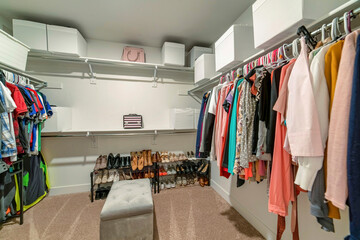 Interior of a walk in closet with ottoman and white storage boxes