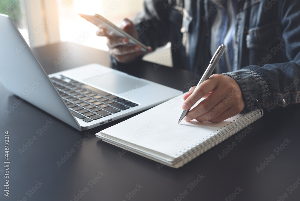 Poster business woman writing on notebook while working on laptop computer and using mobile phone from home