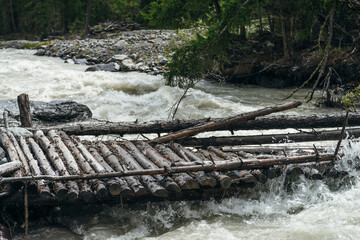 Fast turbulent river with broken bridge in water. Scenic mountain landscape with log bridge across river. Beautiful scenery with wooden bridge over mountain creek. Powerful rapids in mountain river.