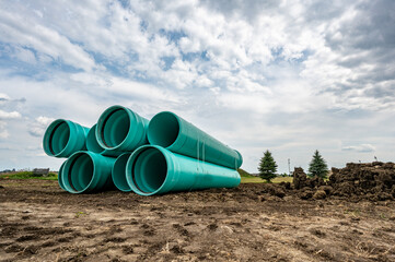 Stacked water main pipe with bell fitting next to an exposed trench for installation