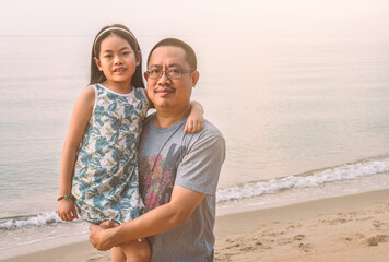 Portrait middle-aged Asian father holding his daughter in his arms on the beach. Blurred background of the sea, blank space for copy and design. © dul_ny
