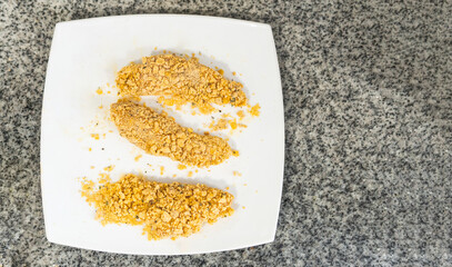 overhead view of breaded chicken breasts on a square white plate ready for frying