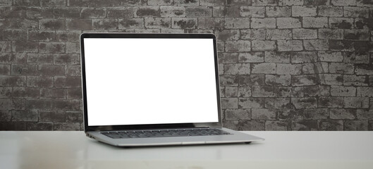 Mock up laptop computer with blank screen on white table with brick wall.
