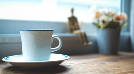 A cup of coffee on wooden table near window.