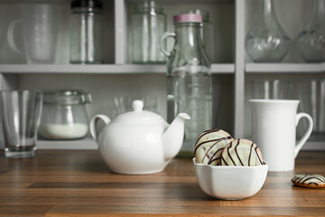 White teapot with tea cup and cookies in white bowl on the countertop of a Scandinavian-style kitchen, teatime and breakfast concept