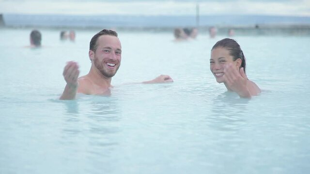Iceland travel. Hot spring geothermal spa. Couple inviting you to join them waving hand welcoming. Romantic couple in love relaxing in hot pool on Iceland