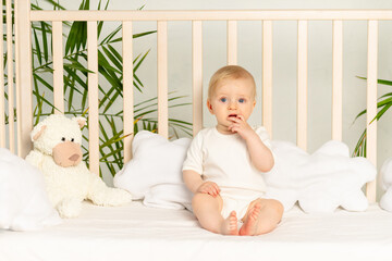 baby boy blonde with blue eyes in a white bodysuit on a bed with cotton underwear at home before...