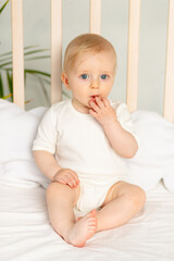 baby boy blonde with blue eyes in a white bodysuit on a bed with cotton underwear at home before...