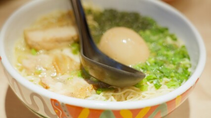 A slow motion closuep footage of a delicious asian noodles soup bowl with a spoon. Japanese ramen with chicken, leak, noodles, broth and boiled egg. Yummy and nutritious food for asian cuisine lovers.