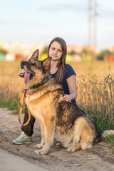 Beautiful young girl with a shepherd dog on the field.