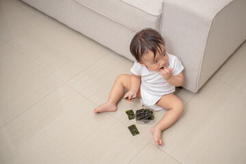A toddler is eating seaweed and sitting on the floor