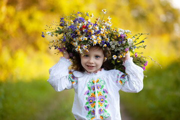 A little girl dressed in an embroidered shirt with a huge wreath of wildflowers. love Ukraine ...