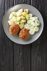 Kotlety Mielone Recipe Traditional Polish Ground Pork Cutlets with boiled potatoes and cucumber salad closeup in the plate on the table. Vertical top view from above