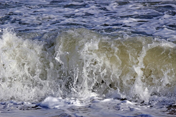 Close-up front view of white foam of an ocean wave breaking near the shore with blue sea water background